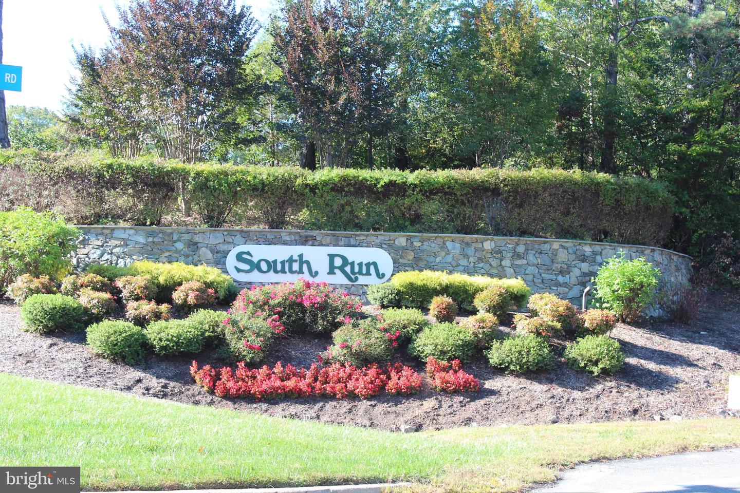South Run neighborhood entrance sign set in a stone wall among landscaped shrubs and flowers.