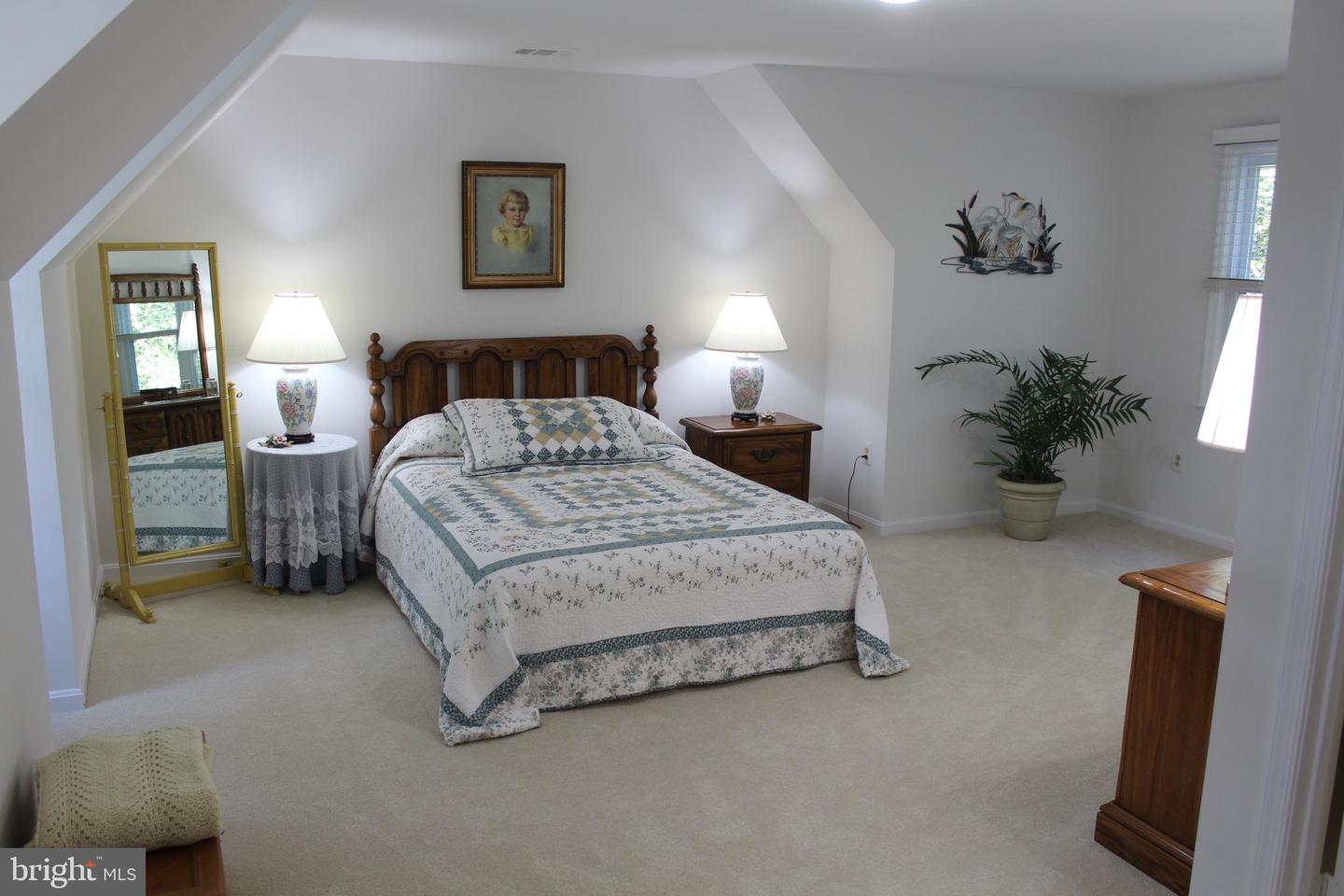 Bedroom with a wooden bed, patterned quilt, matching nightstands, and a full-length mirror.
