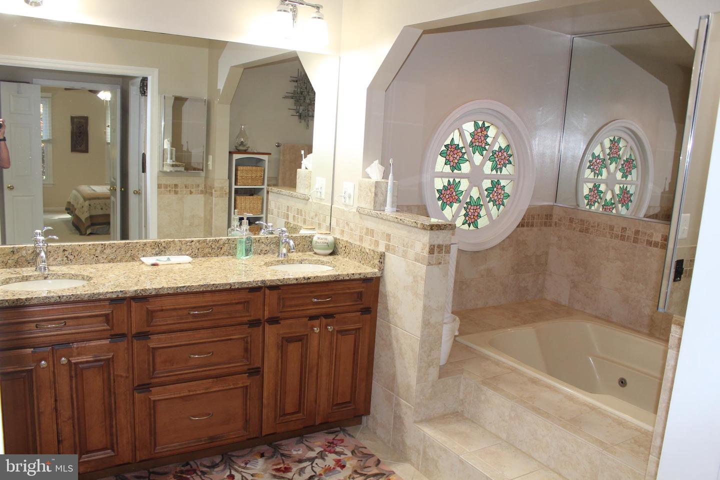 Bathroom with a dark wood double vanity, granite countertop, and tiled soaking tub beneath round stained-glass windows.