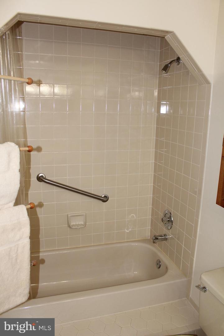 Bathroom with a tiled tub and shower, chrome grab bar, and towel bars.