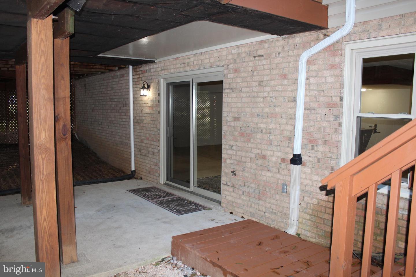 Covered concrete patio with brick walls, sliding glass door, and wooden deck steps.