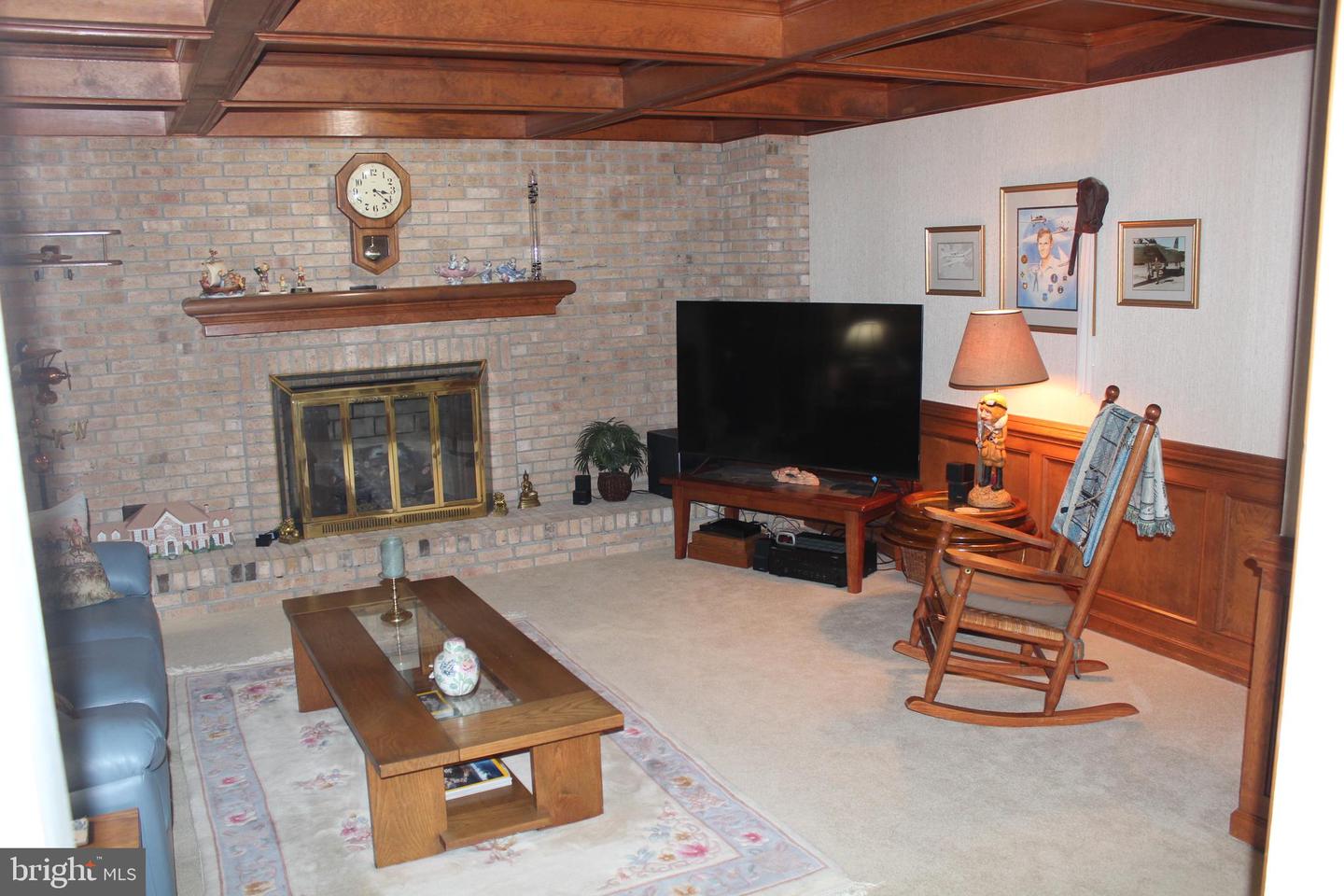 Living room with a brick fireplace, coffered wood ceiling, television, and rocking chair.