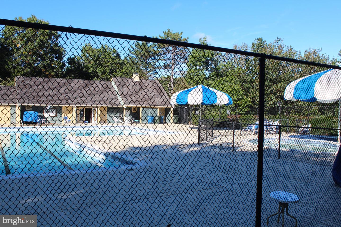Outdoor swimming pool behind a black chain-link fence, with blue-and-white umbrellas and a pool building.