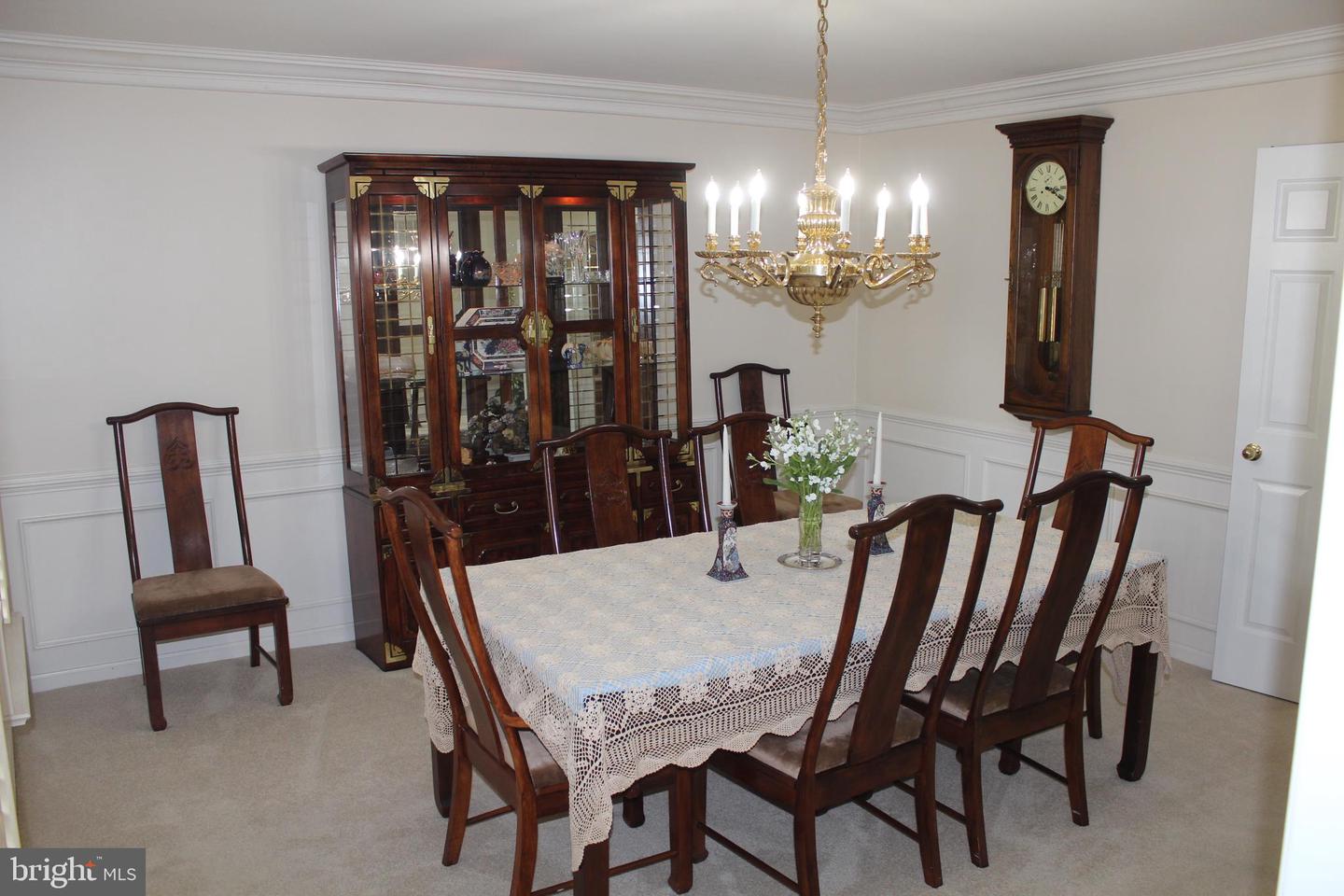 Furnished dining room with a lace-covered table, dark wood china cabinet, grandfather clock, and brass chandelier.