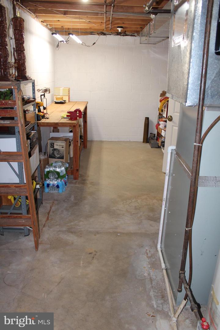 Basement workshop with a concrete floor, workbench, metal shelving, and exposed ceiling joists.