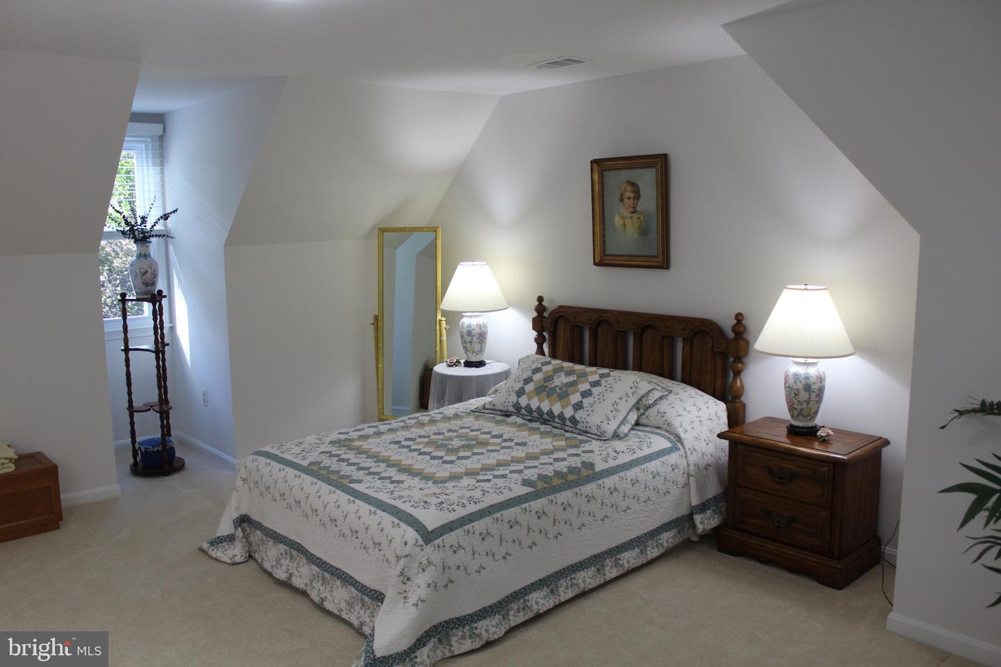 Furnished bedroom with a wooden bed, patterned quilt, matching lamps, and sloped ceiling.