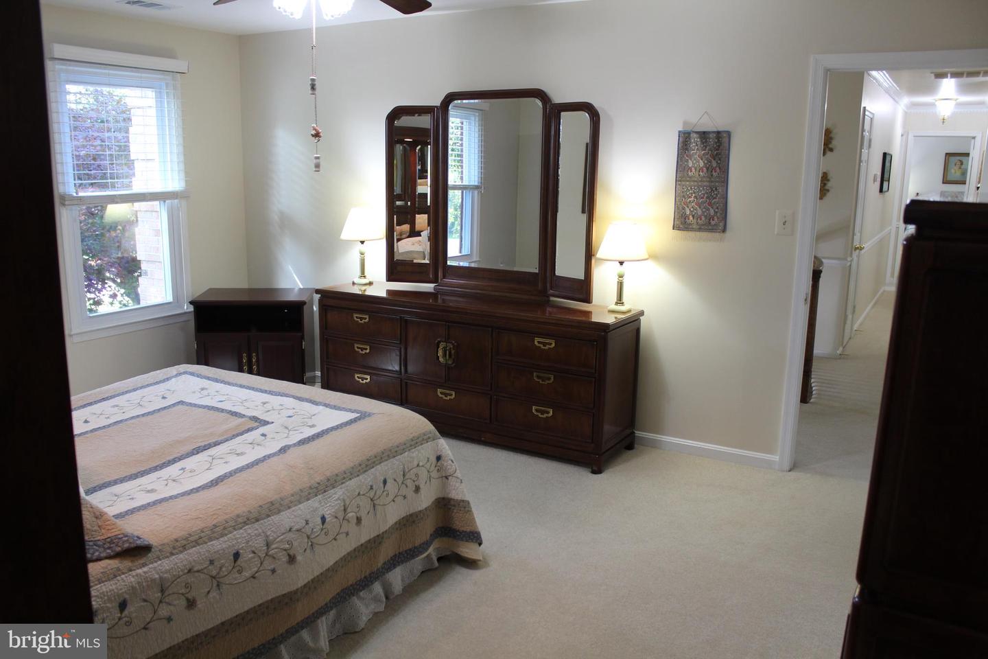 Furnished bedroom with a patterned quilt-covered bed and dark wood dresser with a triple mirror.