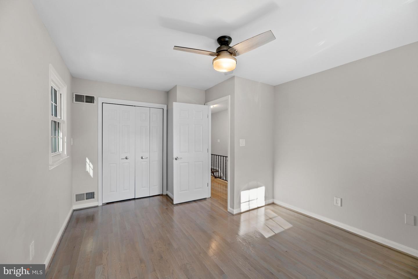 Empty bedroom with wood flooring, double closet doors, and a ceiling fan with a light.