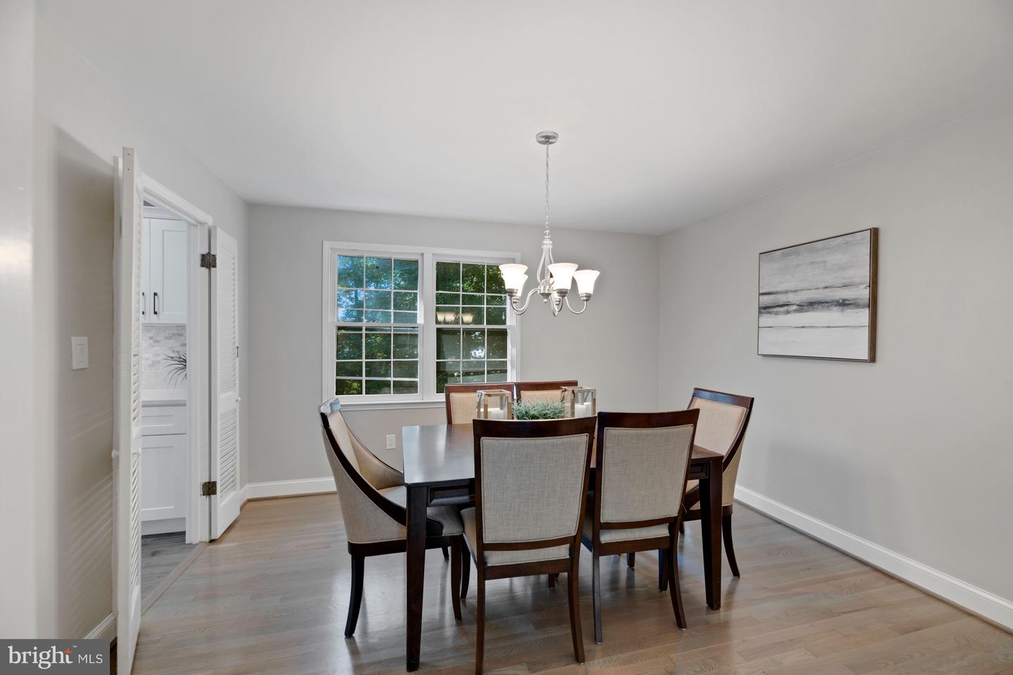 Dining room with a wood table, upholstered chairs, chandelier, and large window.