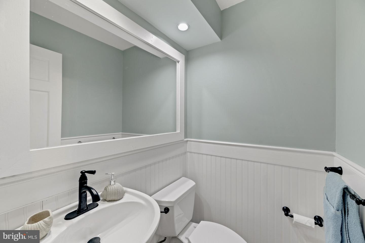 Bathroom with a pedestal sink, black faucet, large mirror, and white beadboard wainscoting.