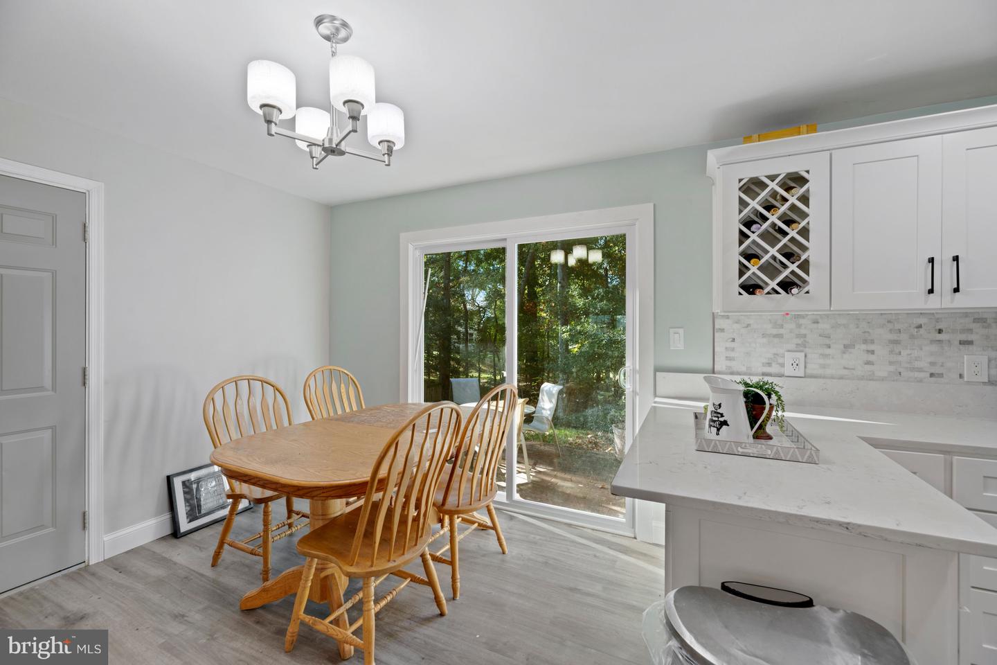 Kitchen and dining area with white cabinetry, a wooden table, and sliding glass doors overlooking trees.