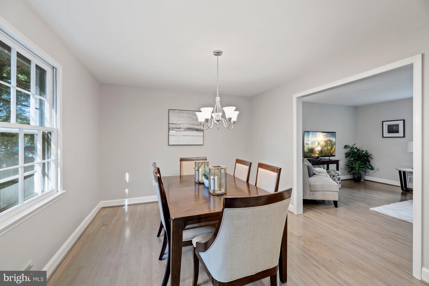 Dining room with a wood table and chandelier, opening to a living room.
