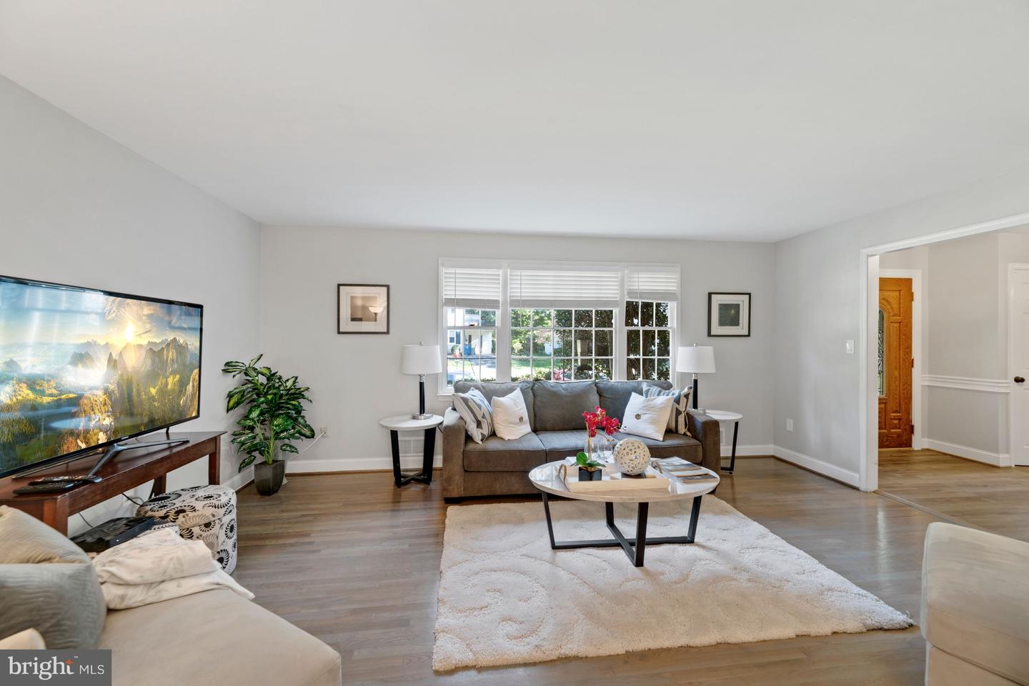 Staged living room with a gray sofa beneath wide windows and a white rug around a coffee table.