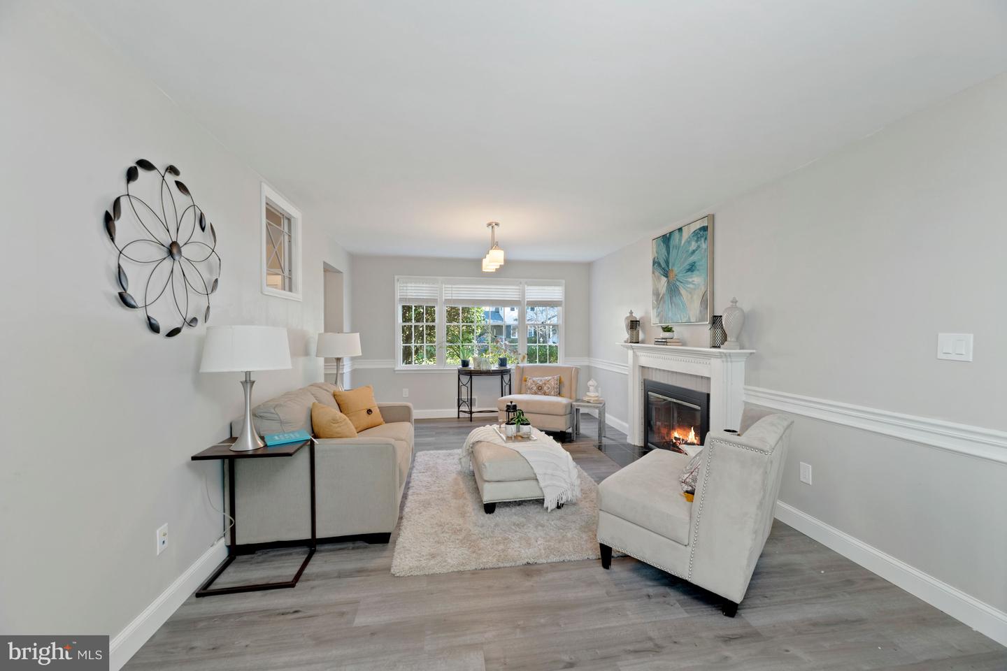 Staged living room with a white fireplace, neutral seating, and large windows.