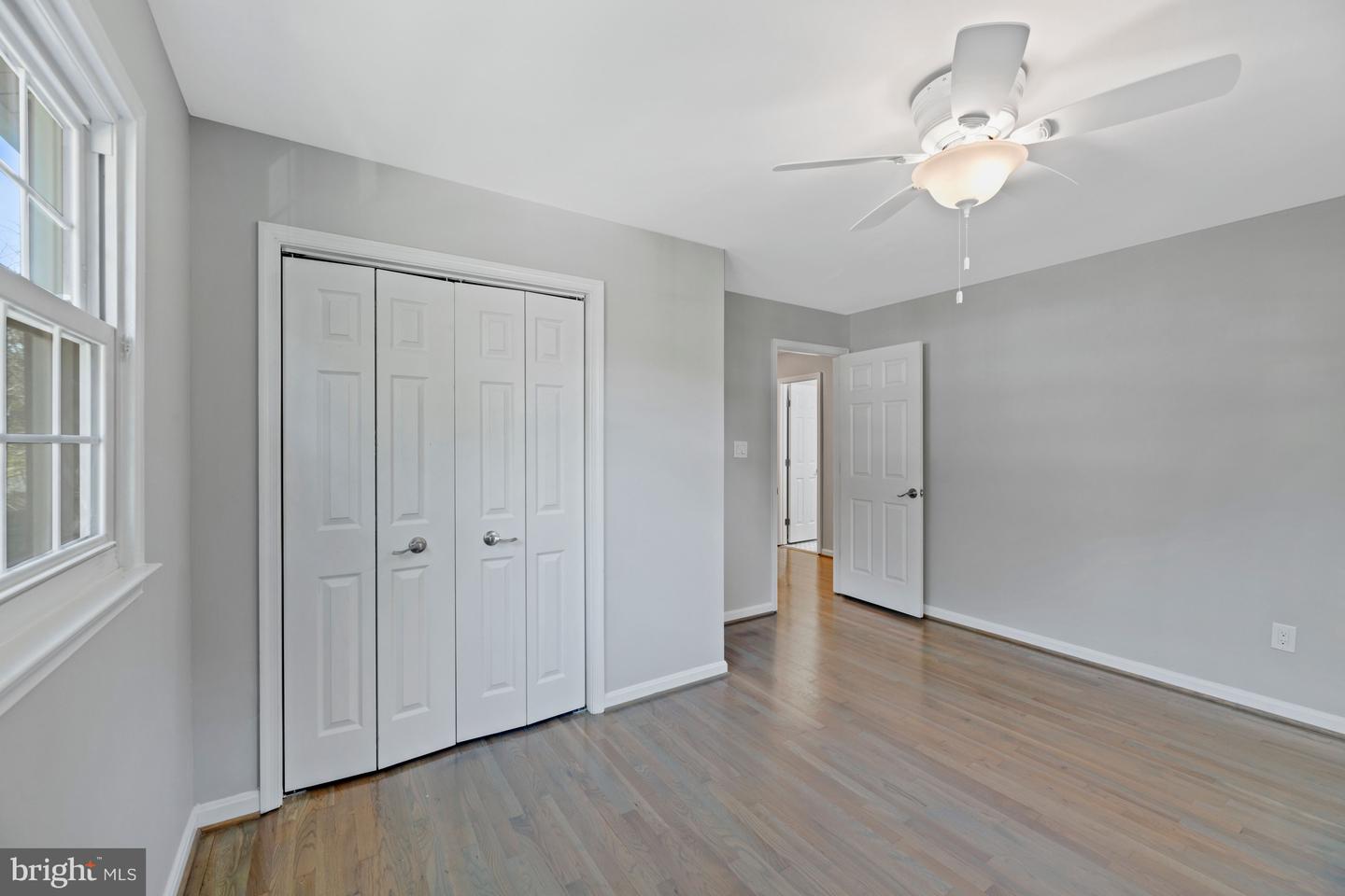 Empty bedroom with hardwood floors, double closet doors, a large window, and a ceiling fan.