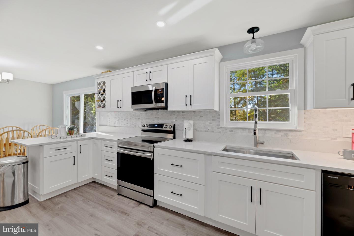 Bright white kitchen with shaker cabinets, stainless steel appliances, and a large sink beneath a window.