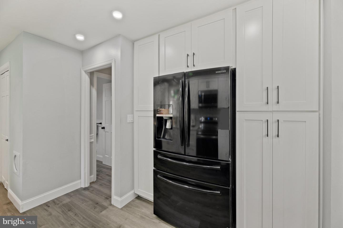 Kitchen with a black Samsung refrigerator, tall white cabinets, and gray wood-look flooring.