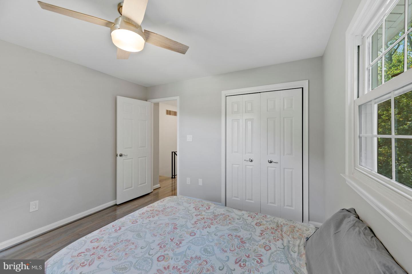 Bedroom with patterned bedspread, white closet doors, and a large window overlooking trees.