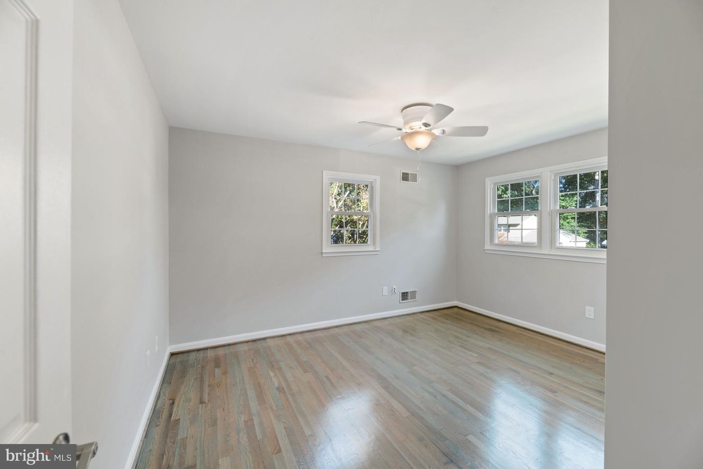 Empty room with hardwood floors, multiple windows, and a ceiling fan with light.