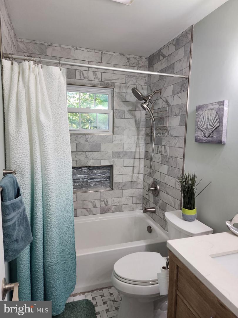 Bathroom with a gray tile tub surround, built-in niche, and window above the bathtub.