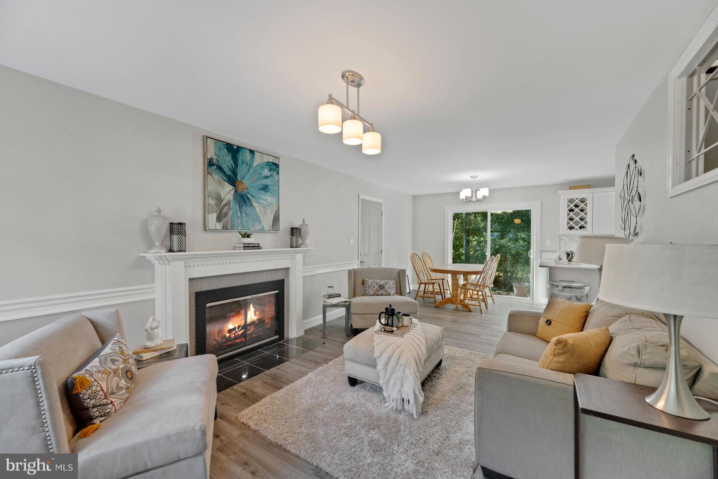 Living room with a lit fireplace, neutral seating, and an adjoining dining area beside glass doors.