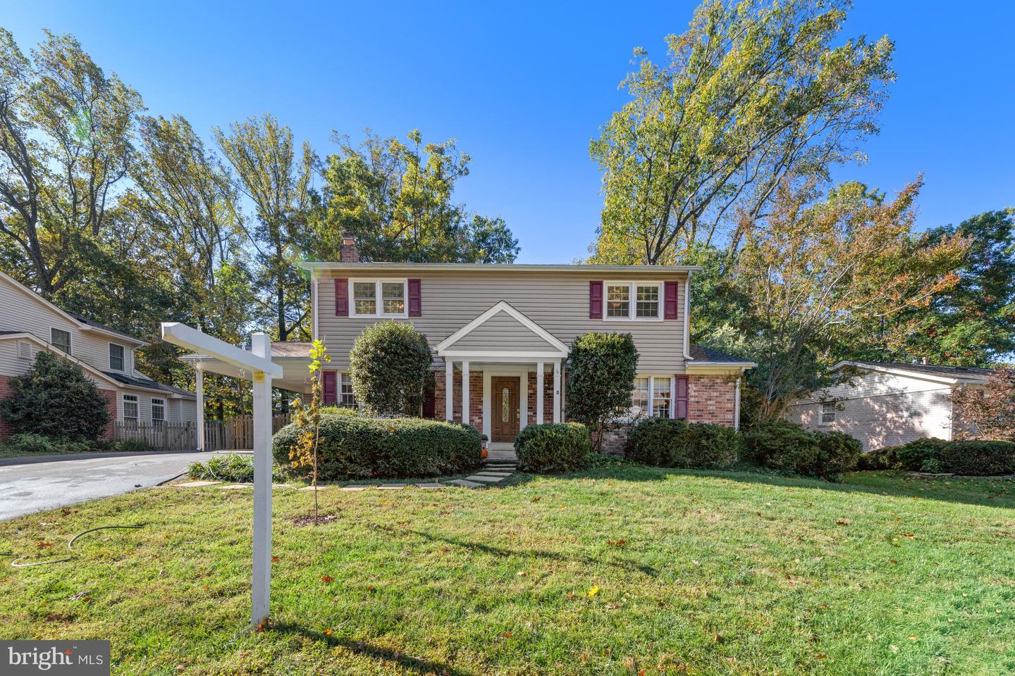 Two-story beige and brick home with burgundy shutters, covered entry, and a broad front lawn.
