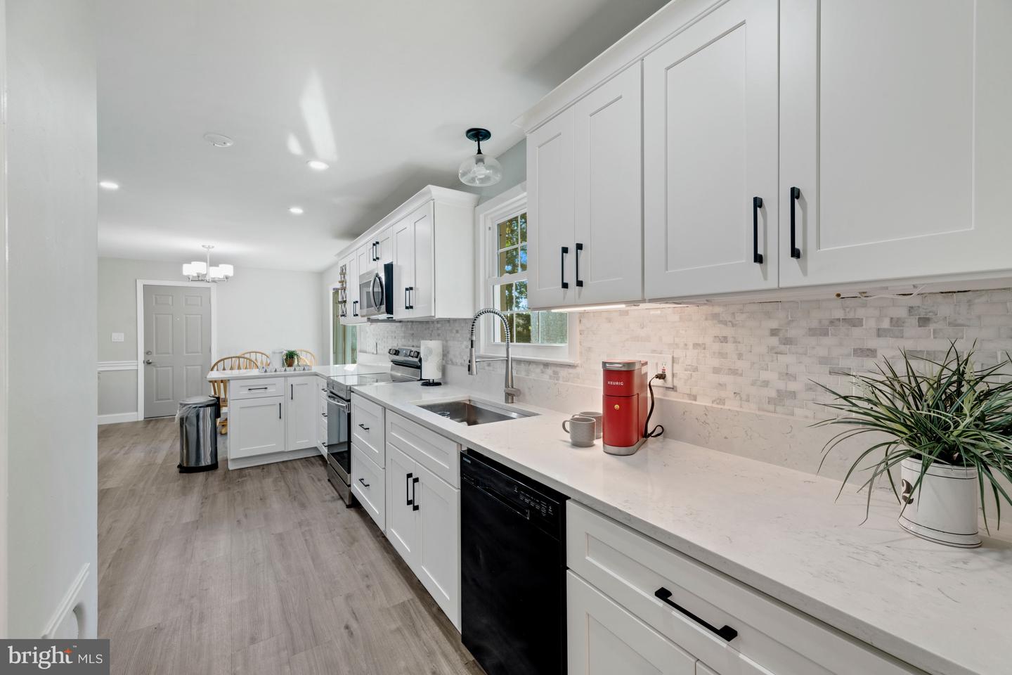 Bright white kitchen with shaker cabinets, gray tile backsplash, and a long stone countertop.