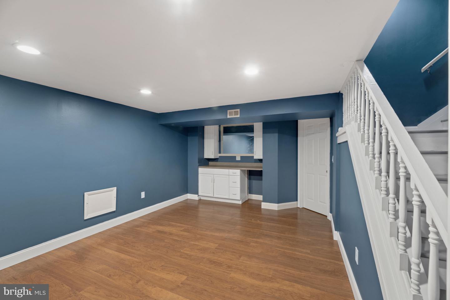 Finished basement with blue walls, wood flooring, a small kitchenette, and a white staircase.