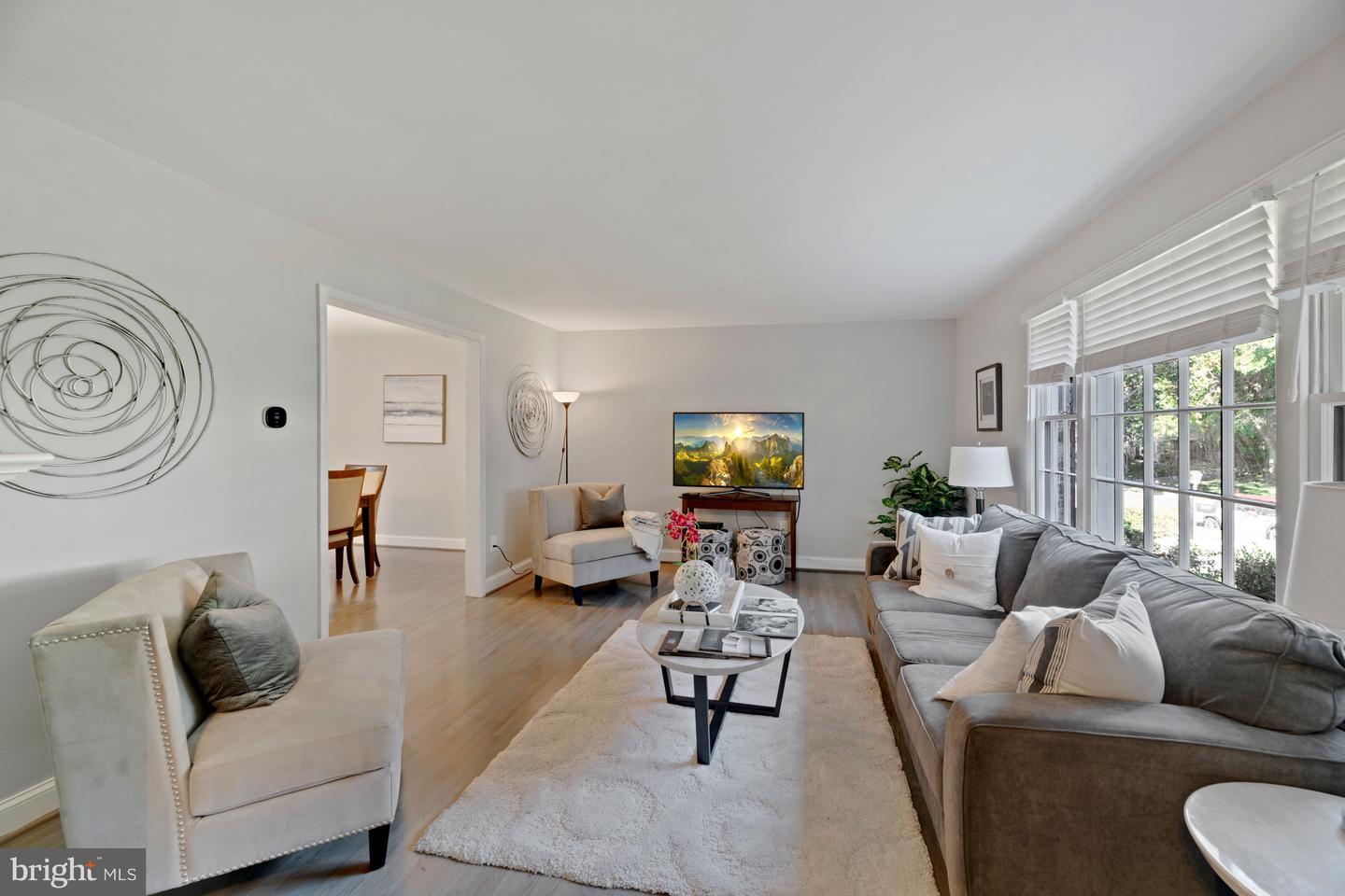 Staged living room with gray and cream sofas, an oval coffee table, and large windows with blinds.