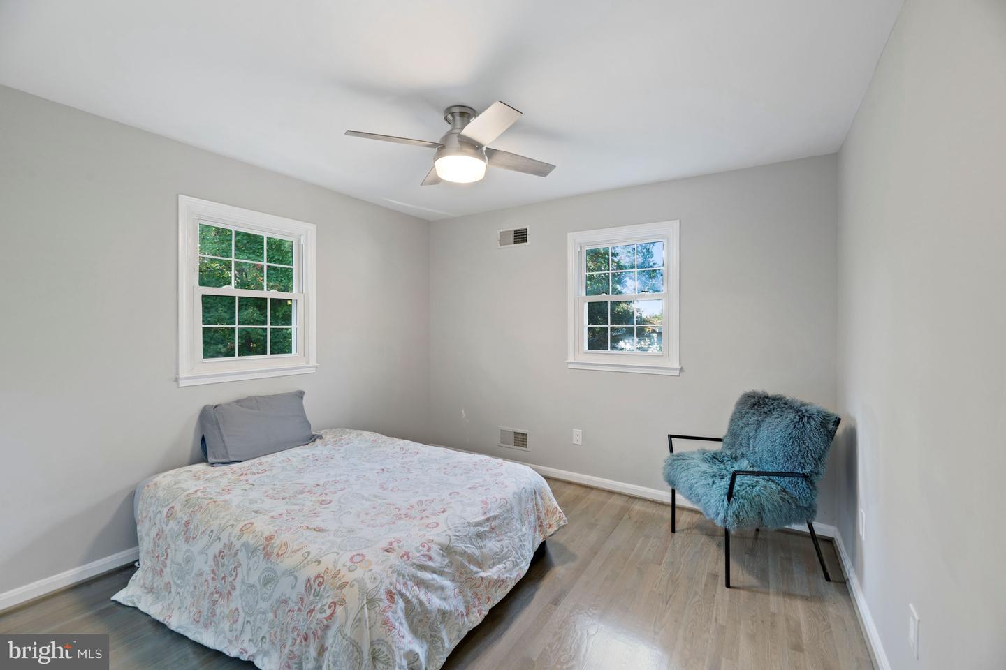Furnished bedroom with two windows, a patterned bedspread, and a blue accent chair.