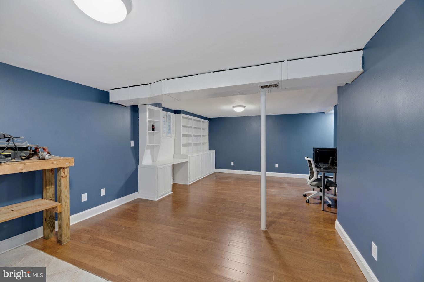 Finished basement with blue walls, hardwood floors, white built-ins, and a small desk area.
