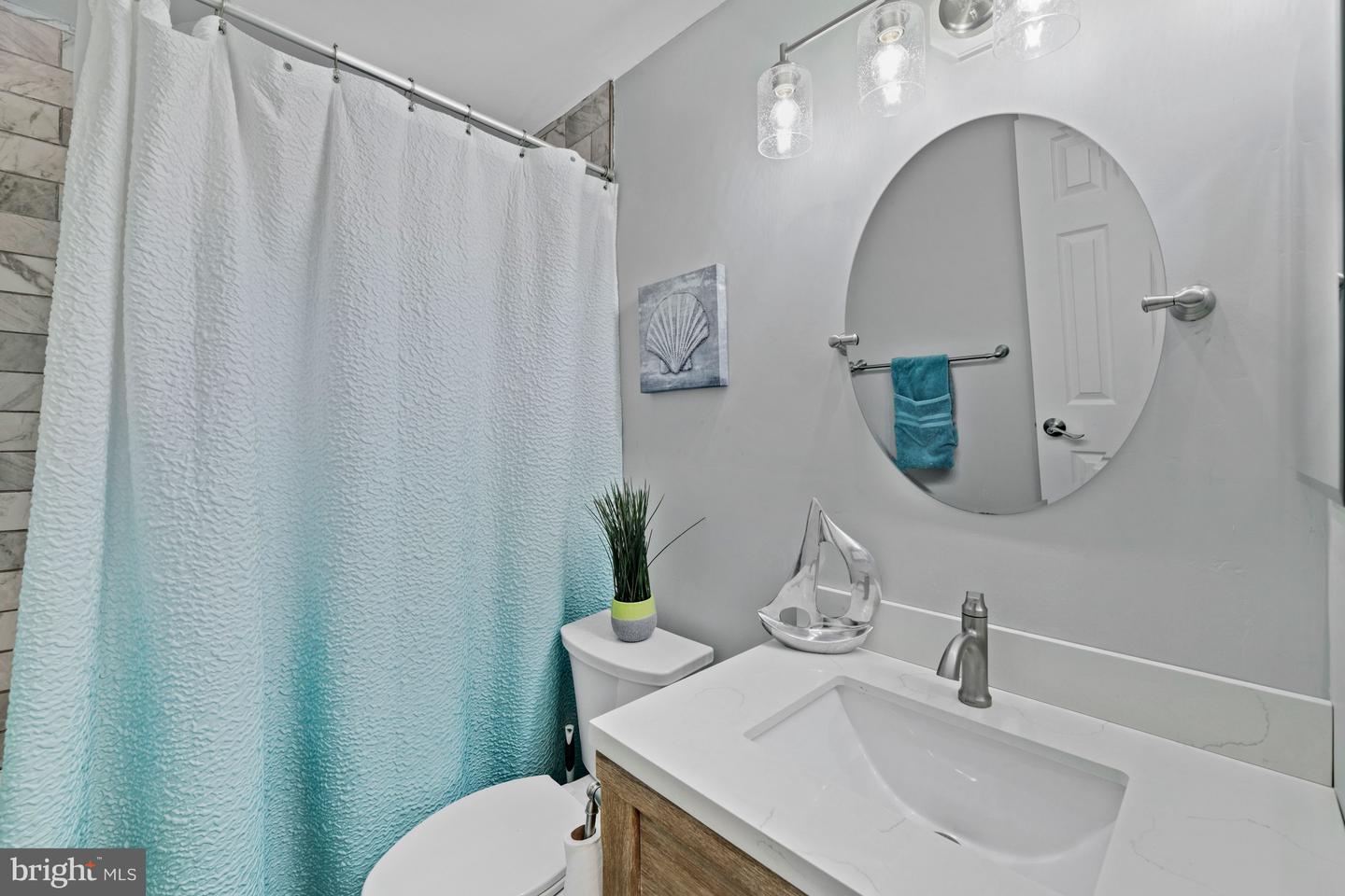 Bathroom with a turquoise shower curtain, white vanity, and large oval mirror.