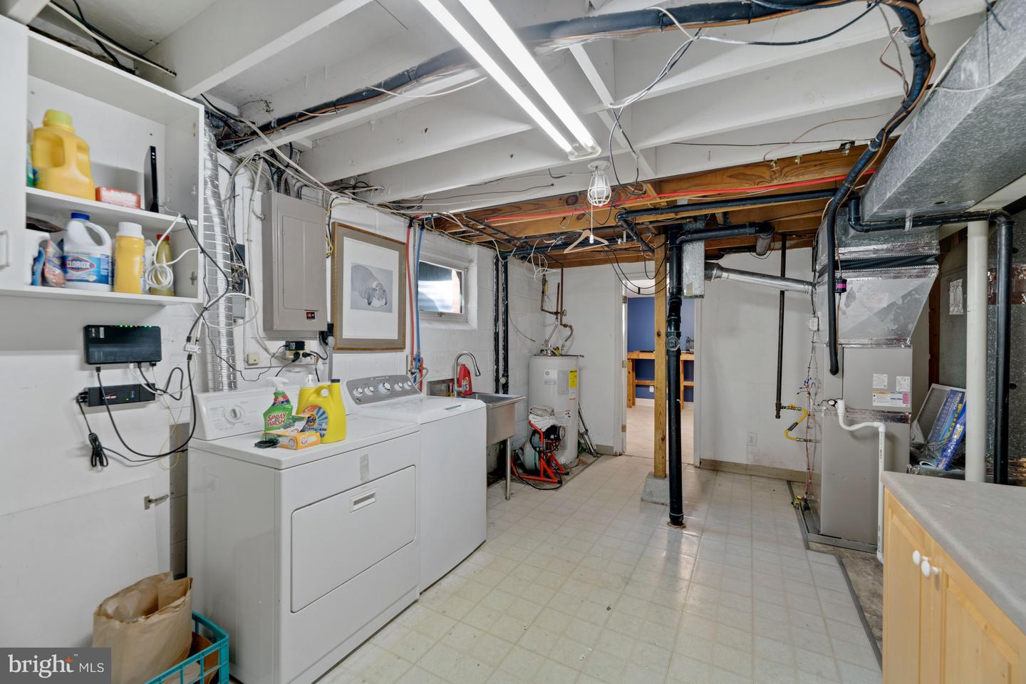 Basement laundry room with washer and dryer beneath exposed beams, ducts, pipes, and wiring.