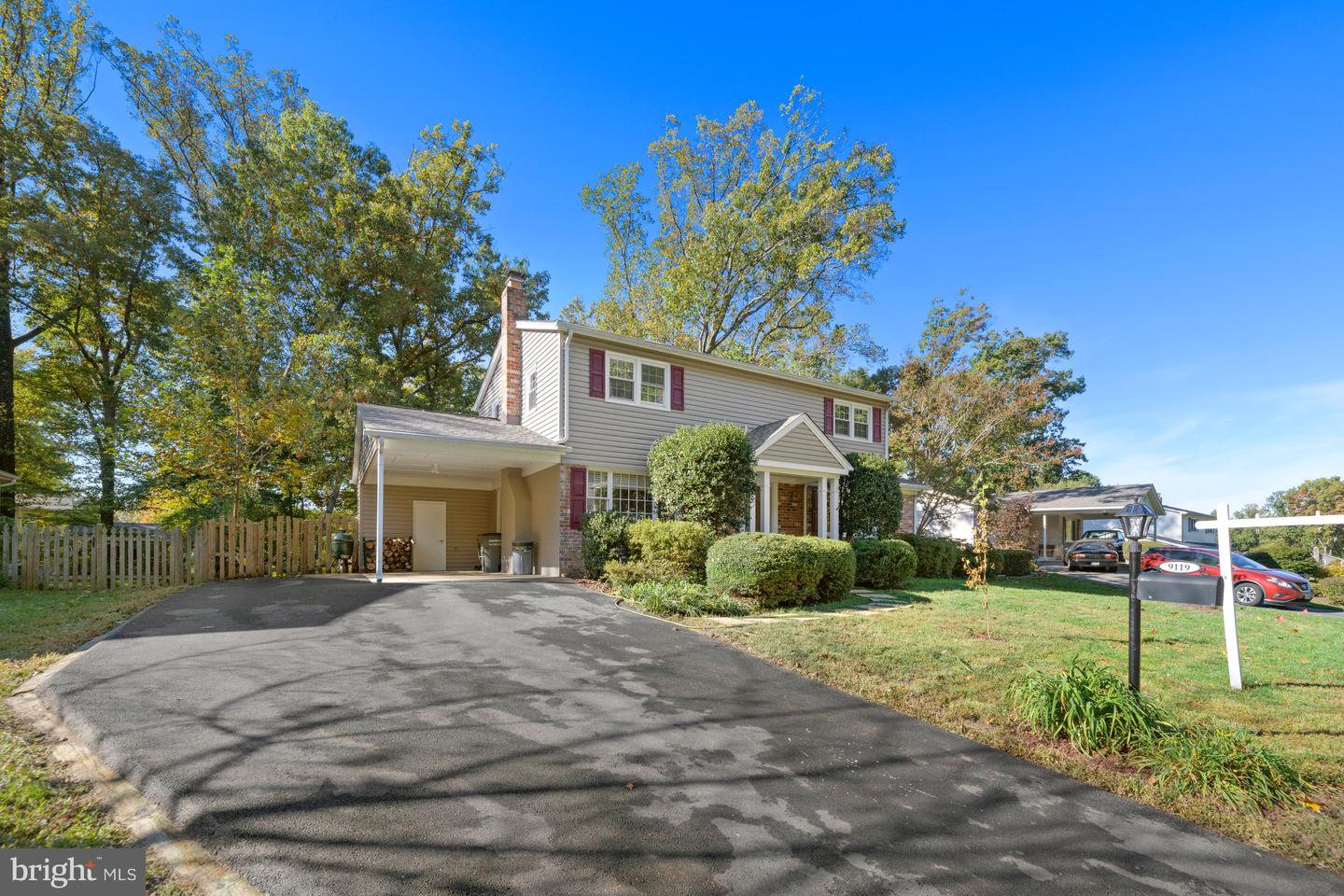 Two-story beige home with brick accents, burgundy shutters, and a wide driveway.