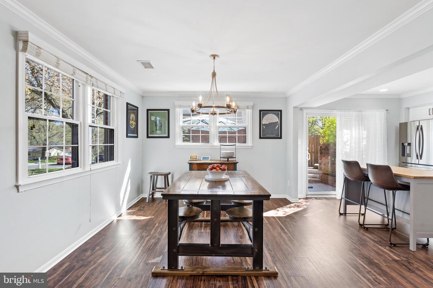 Dining room with a dark wood table, large windows, hardwood floors, and an adjoining kitchen breakfast bar.