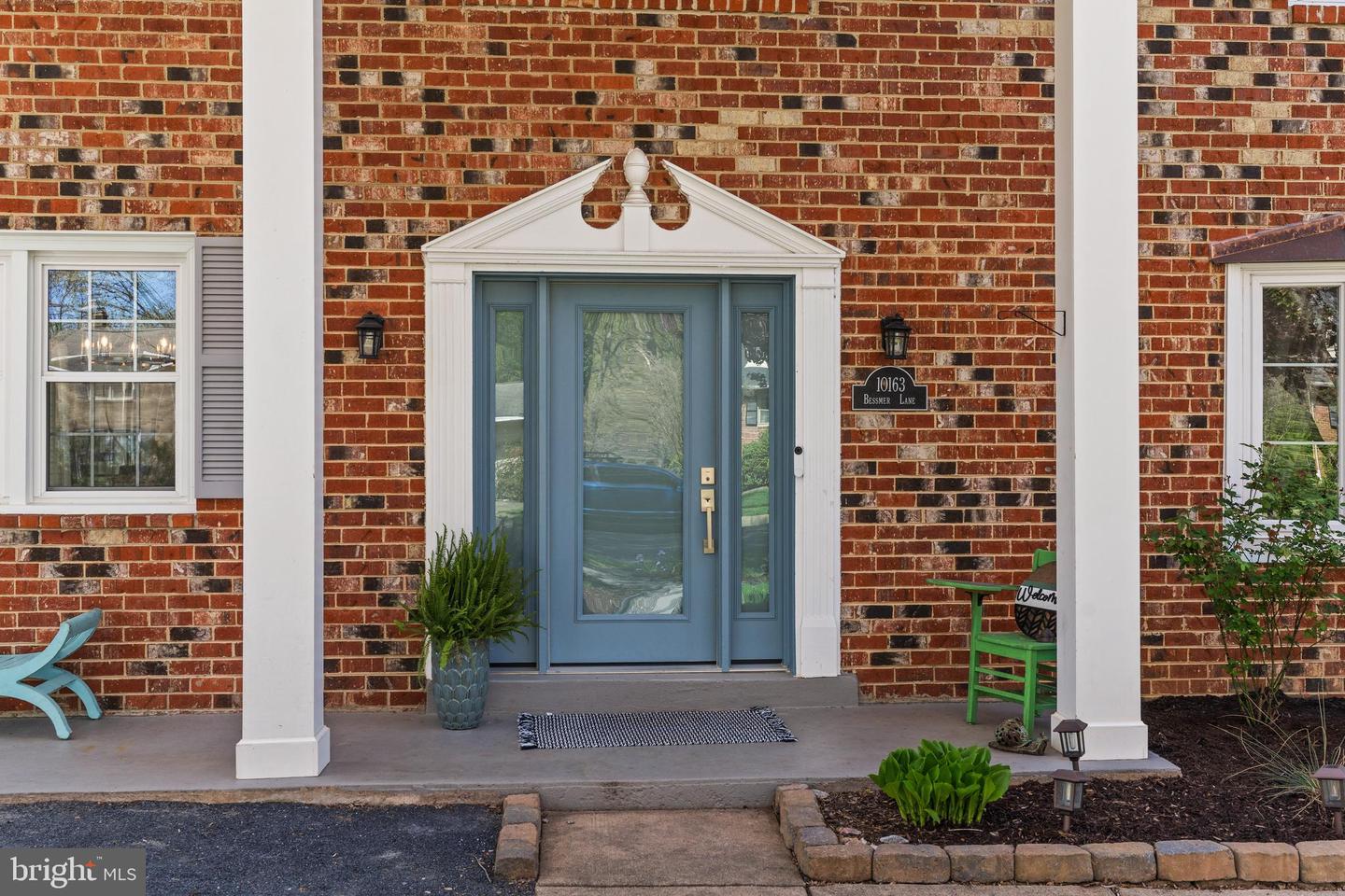Brick home entrance with a blue front door, white portico, and address plaque.