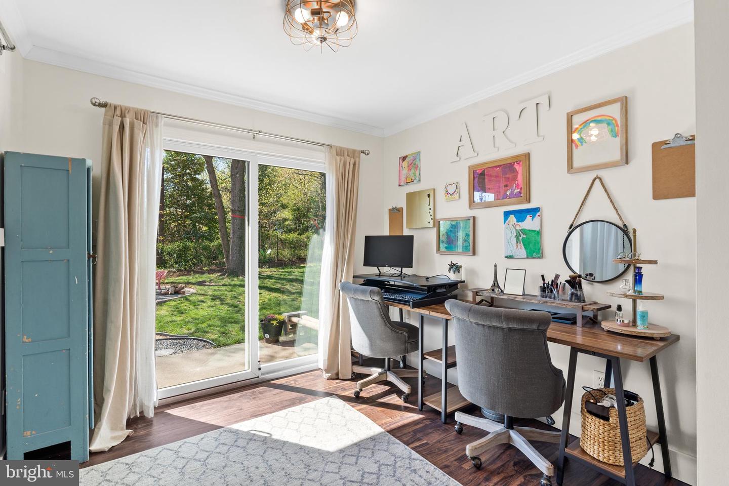 Home office with two desks and colorful artwork beside sliding glass doors to the backyard.