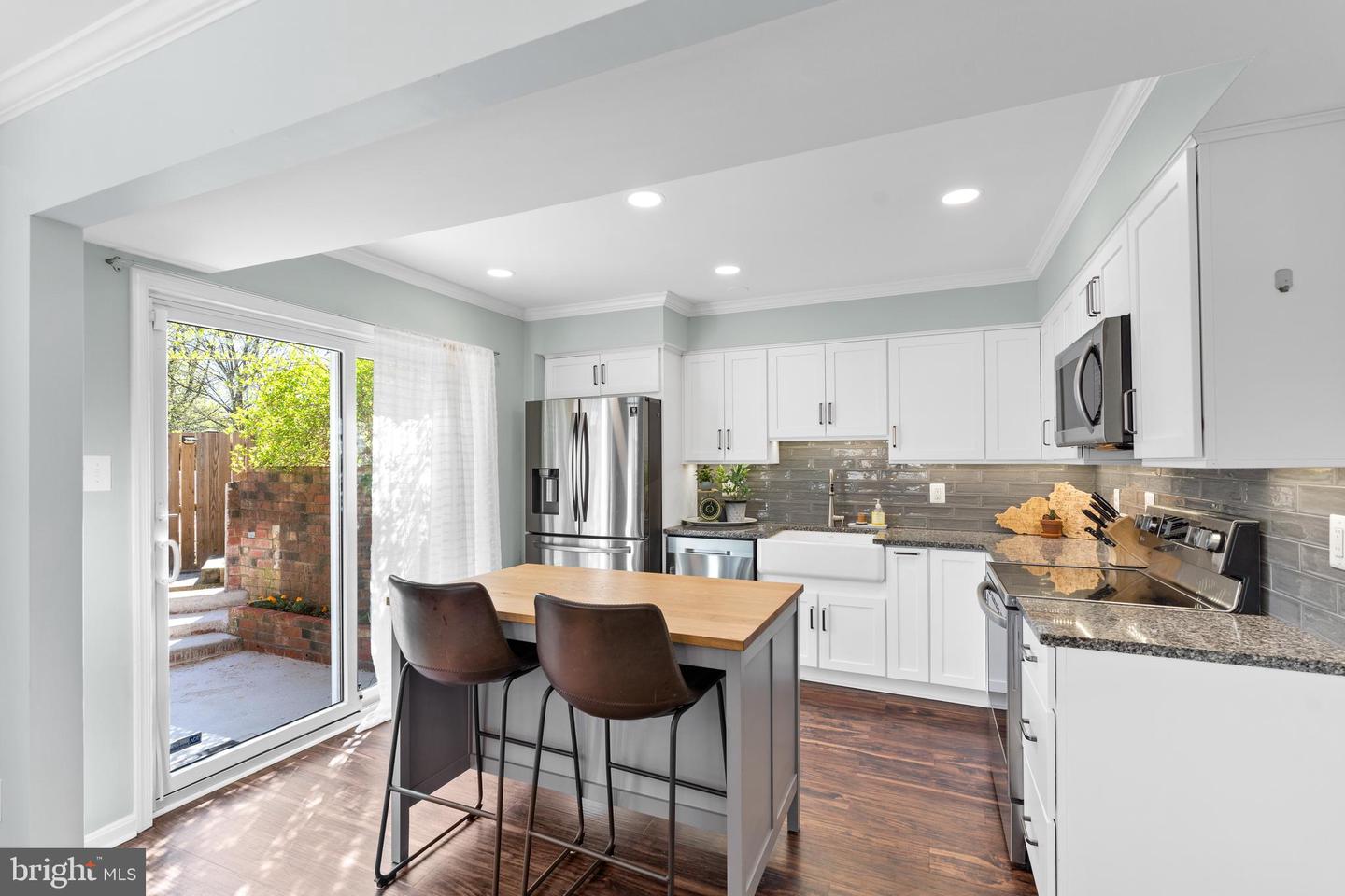 Kitchen with white cabinets, stainless appliances, and a wood-topped island beside a sliding glass door.