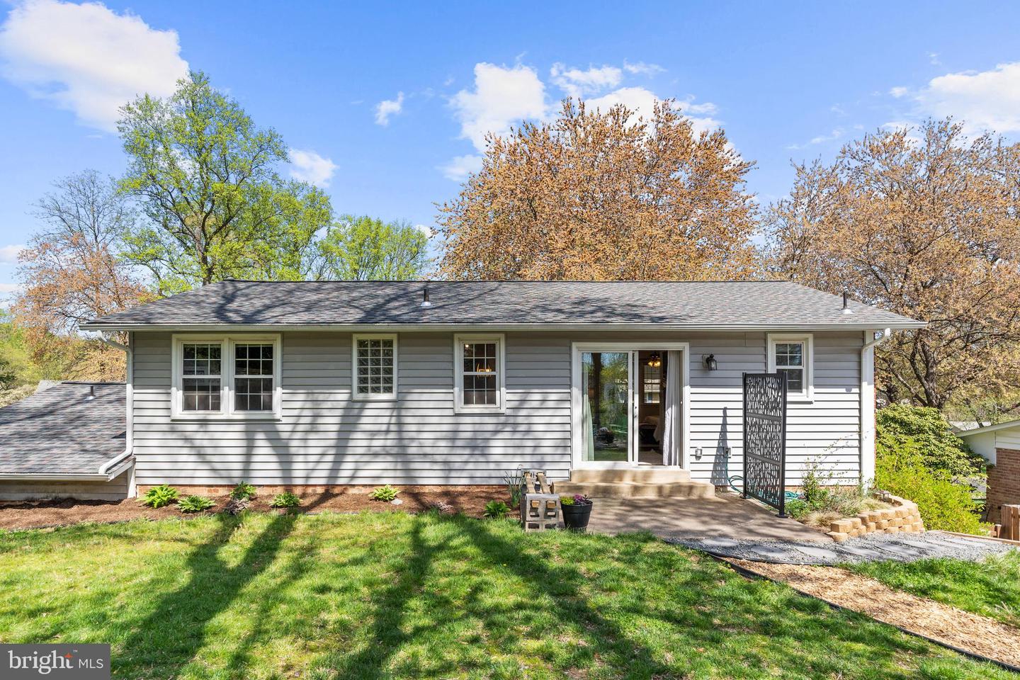 Rear of a gray-sided home with a sliding glass door, patio steps, and a tree-shaded lawn.