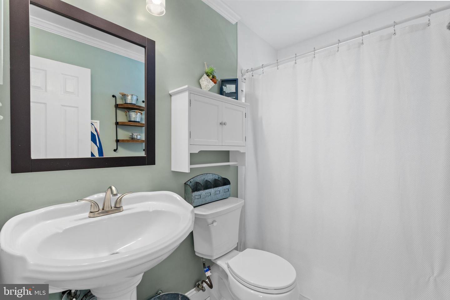 Bathroom with a pedestal sink, wall-mounted cabinet, and white shower curtain.