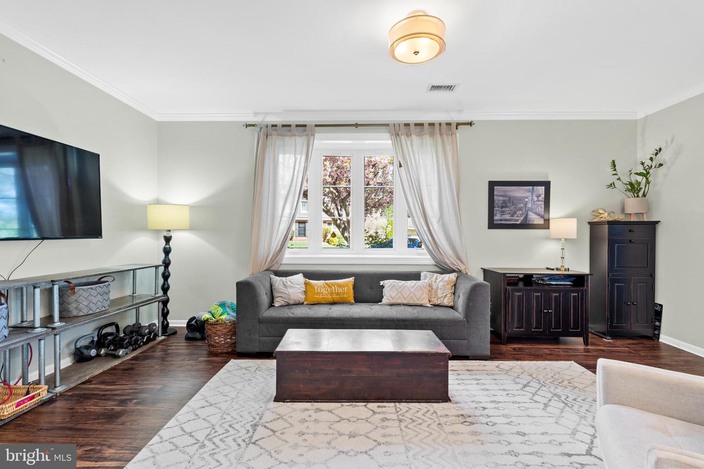 Living room with a gray sofa, wooden coffee table, and large window overlooking flowering trees.
