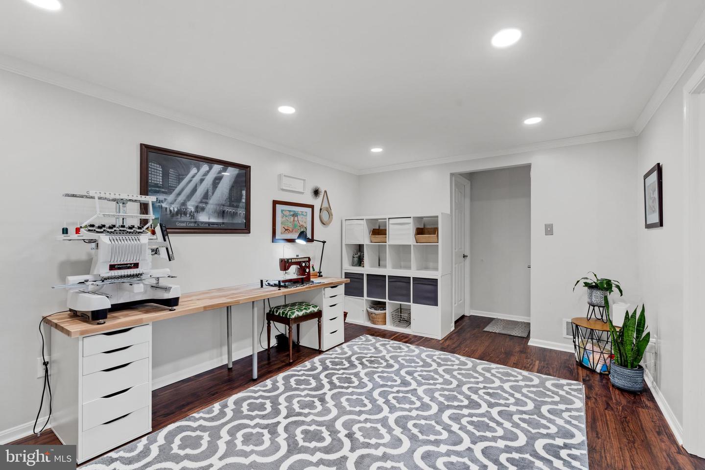 Craft room with embroidery and sewing machines on a long worktable and a patterned rug.