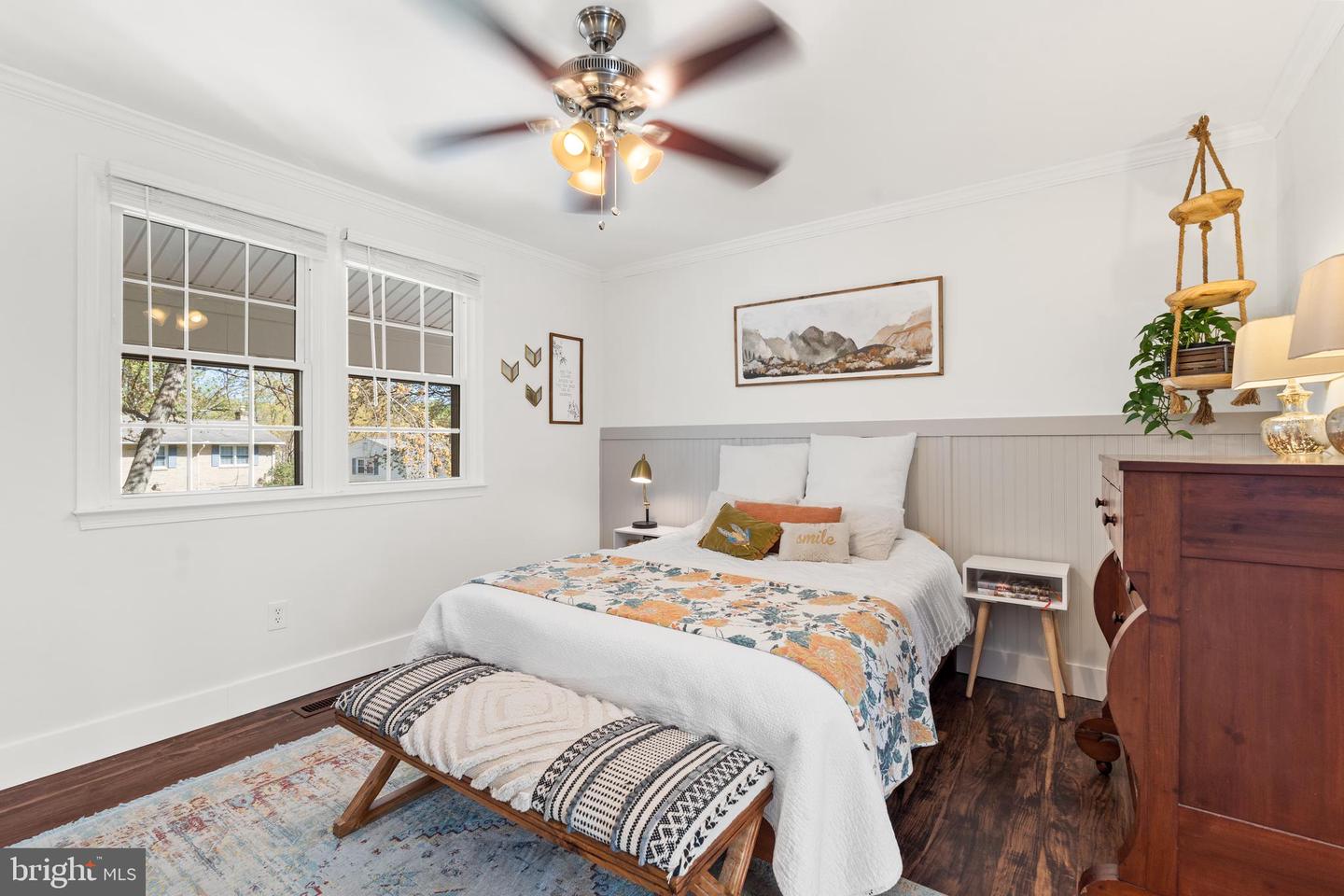 Furnished bedroom with a floral coverlet, patterned bench, and two large windows.