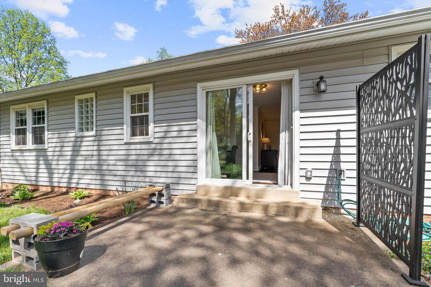 Rear of a gray-sided home with a concrete patio, sliding glass door, and decorative privacy screen.