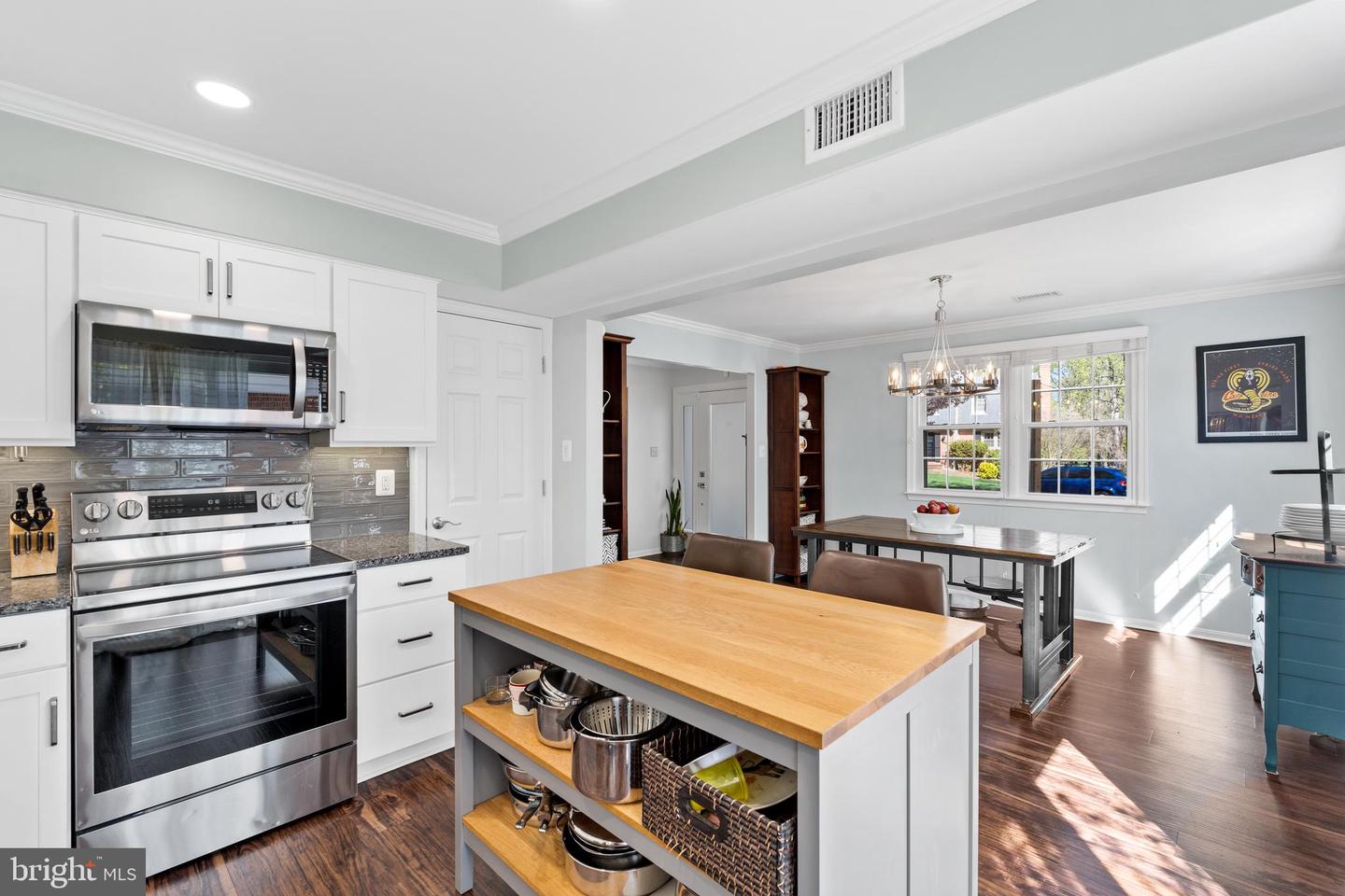 Open kitchen with white cabinets, stainless steel appliances, and a wood-top island beside a window-lit dining area.
