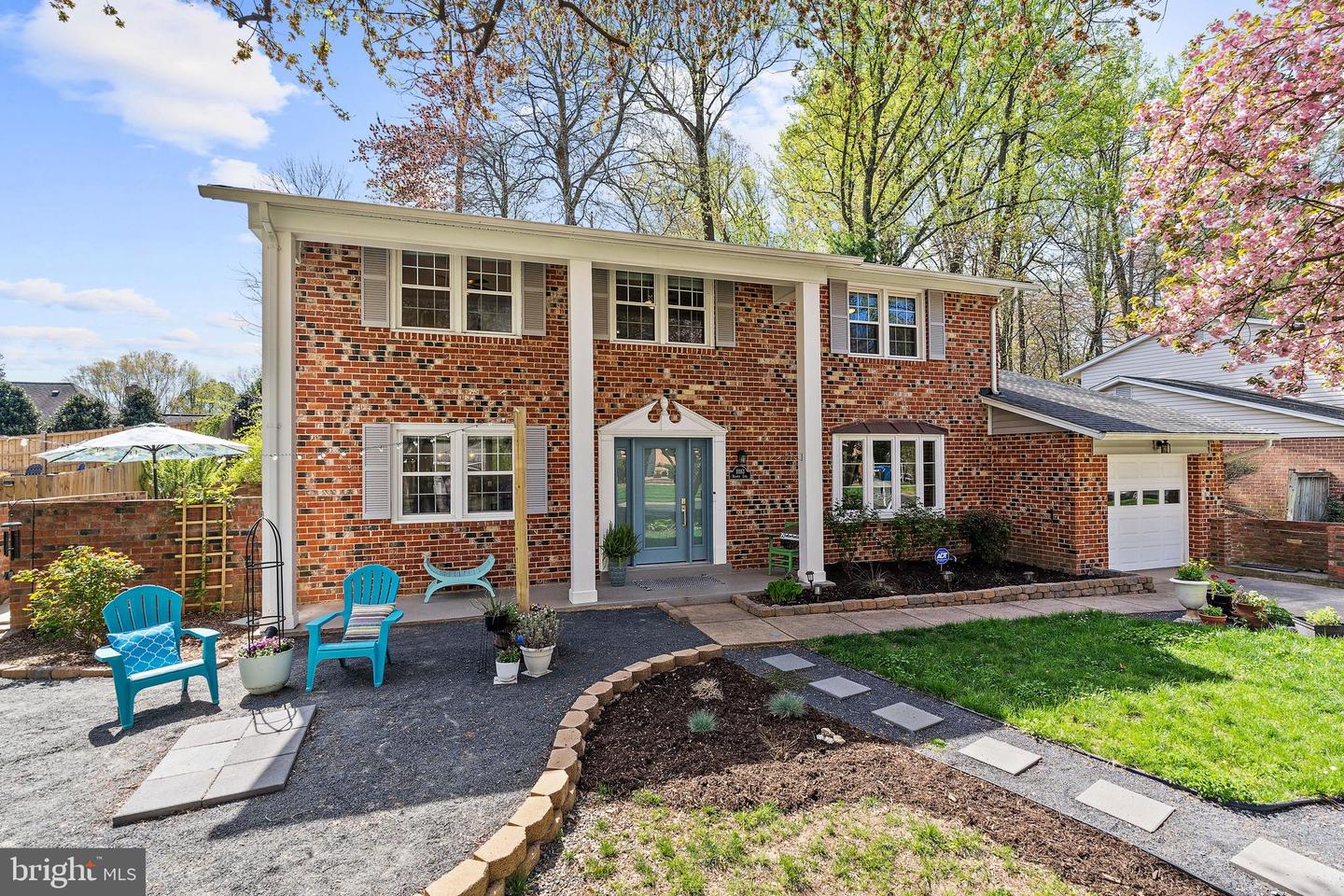 Two-story brick house with a covered entry, curved walkway, landscaped yard, and turquoise patio chairs.