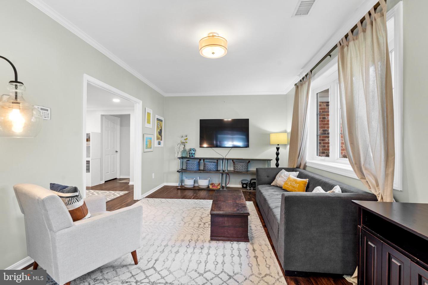 Living room with gray sofas, a patterned rug, and tall windows with beige curtains.