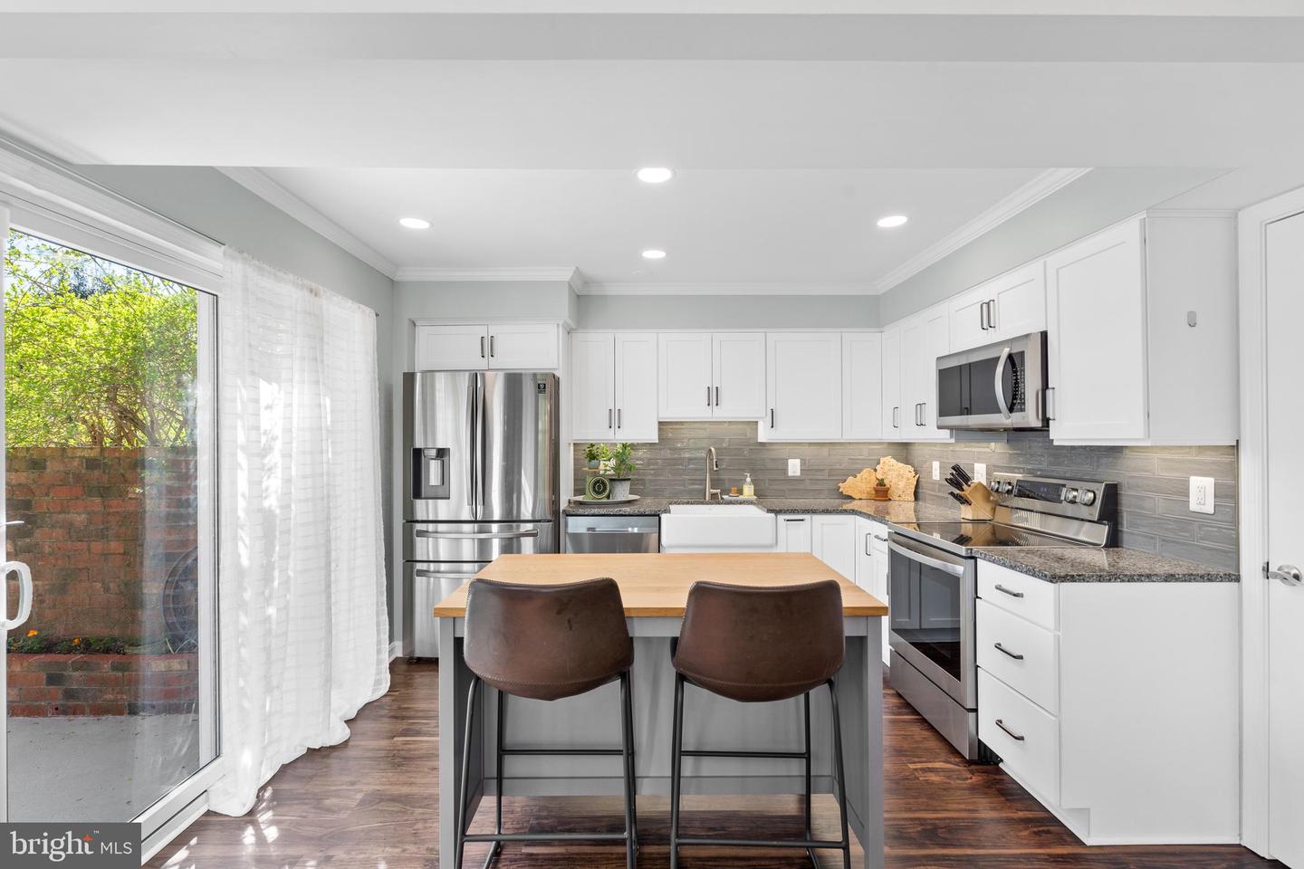 Bright kitchen with white cabinetry, stainless appliances, and a wood-topped island beside sliding glass doors.