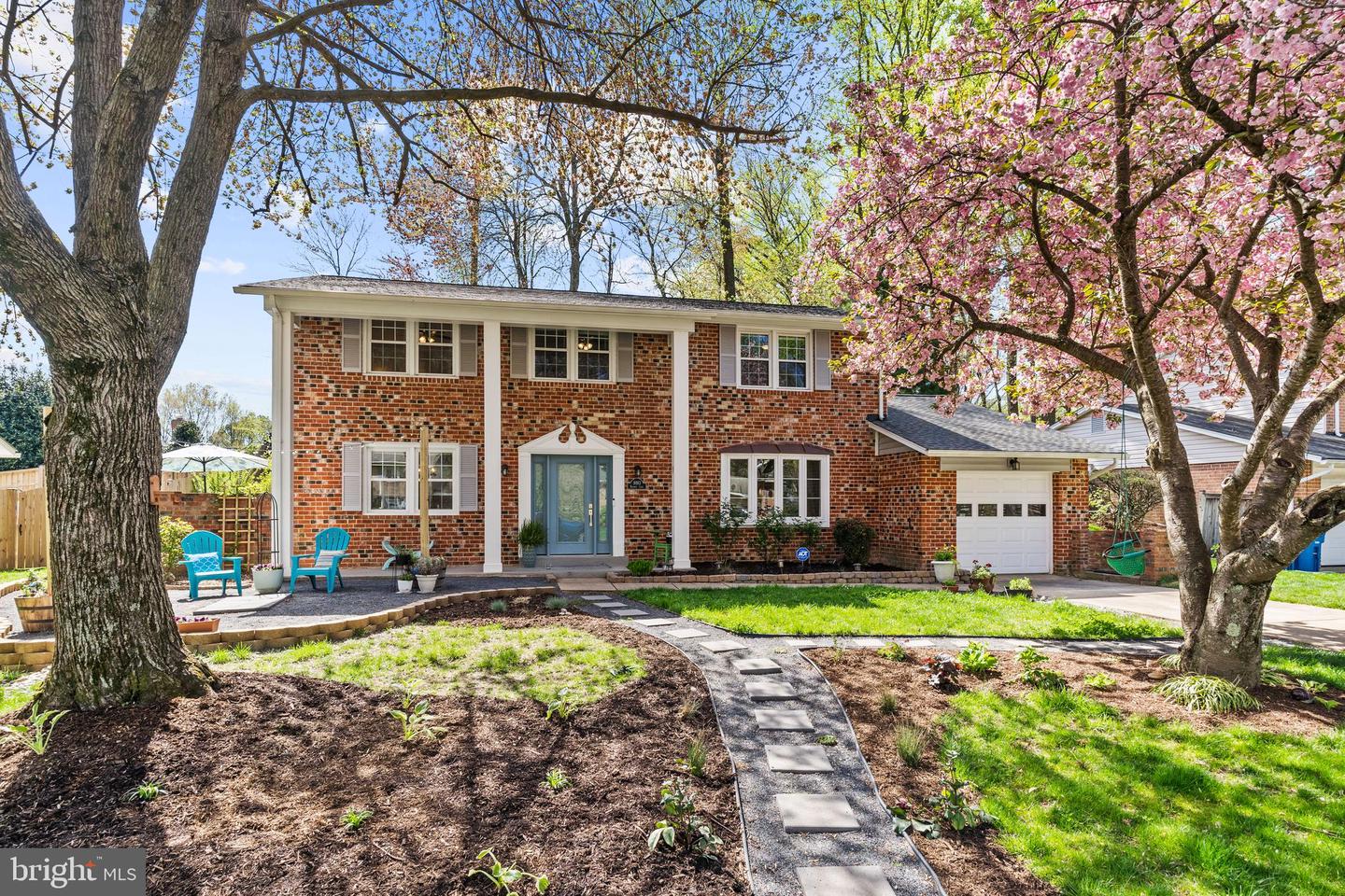 Brick two-story home with a blue front door, attached garage, and flowering spring trees.
