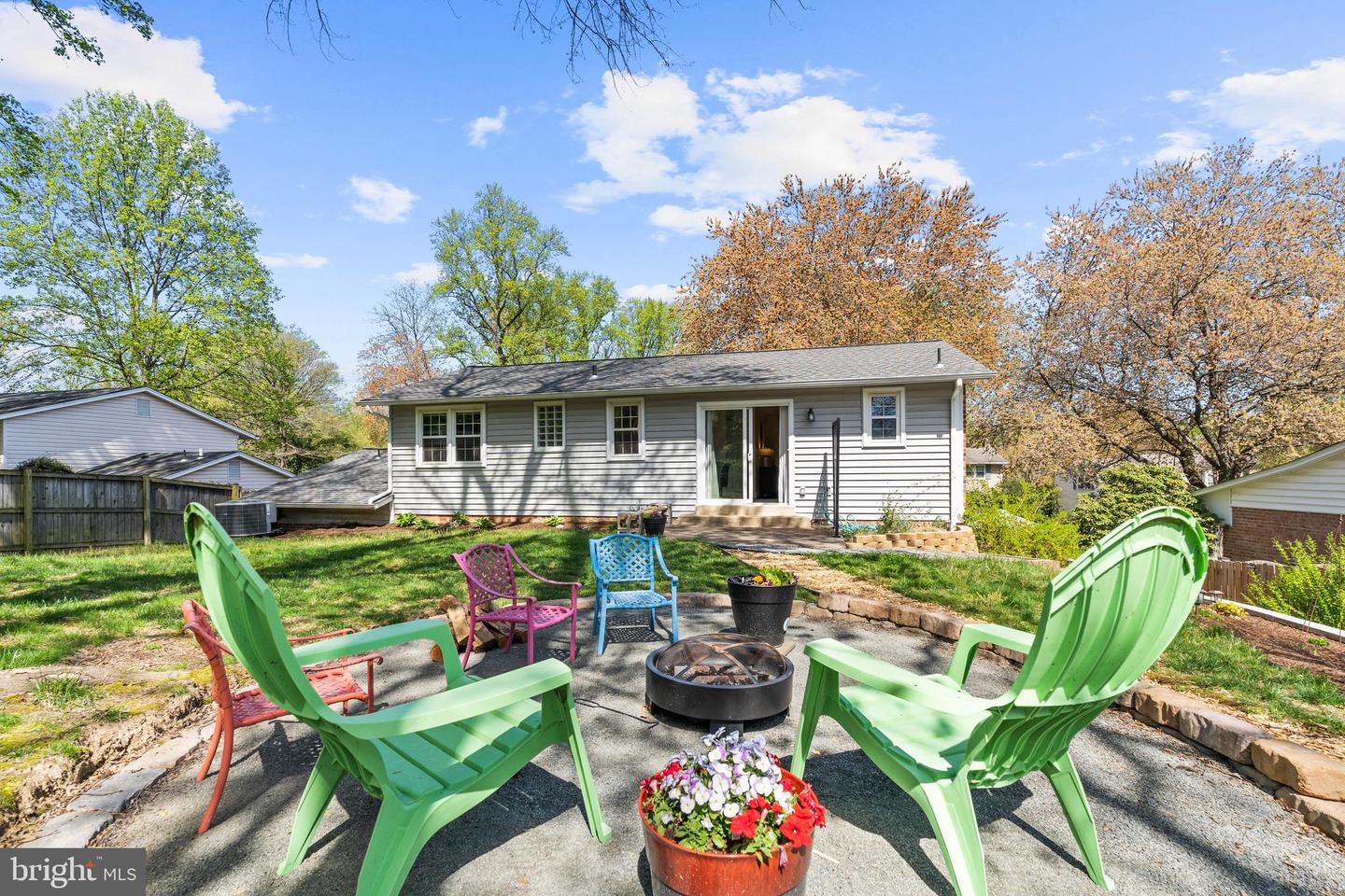 Rear of a gray-sided house with a patio, colorful chairs, and a fire pit.
